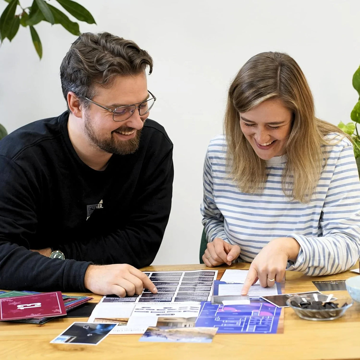 Zwei Personen sitzen an einem Tisch und schauen sich Fotos und Dokumente an