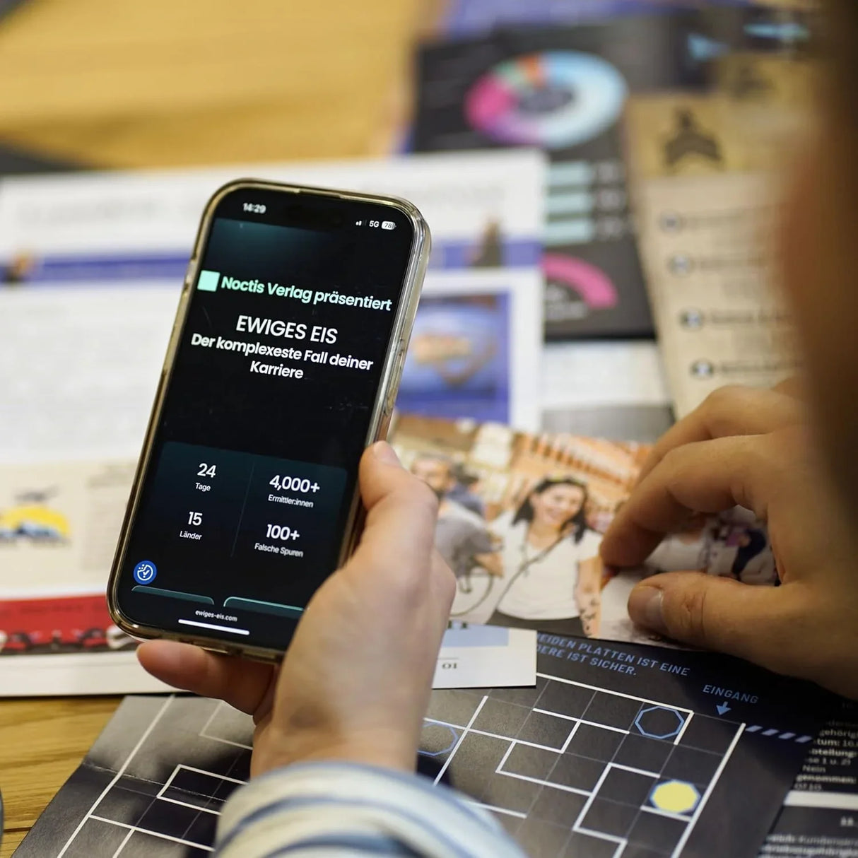 Person hält Smartphone mit Spielanzeige Ewiges Eis über Spielbrett