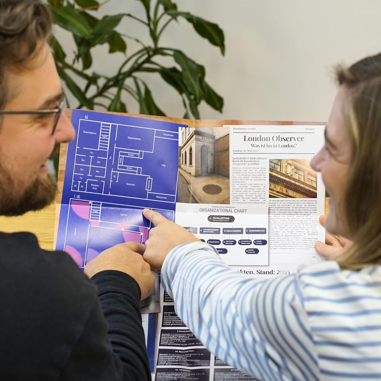 Zwei Personen zeigen auf einen Plan und ein Organigramm in einem Magazin