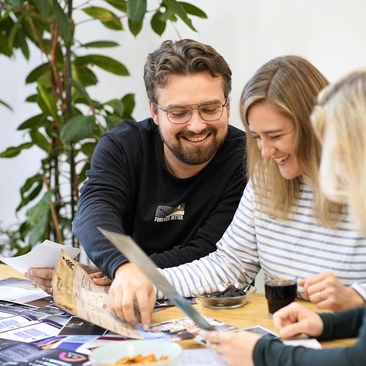 Drei Personen sitzen an einem Tisch und schauen sich Dokumente und Fotos an