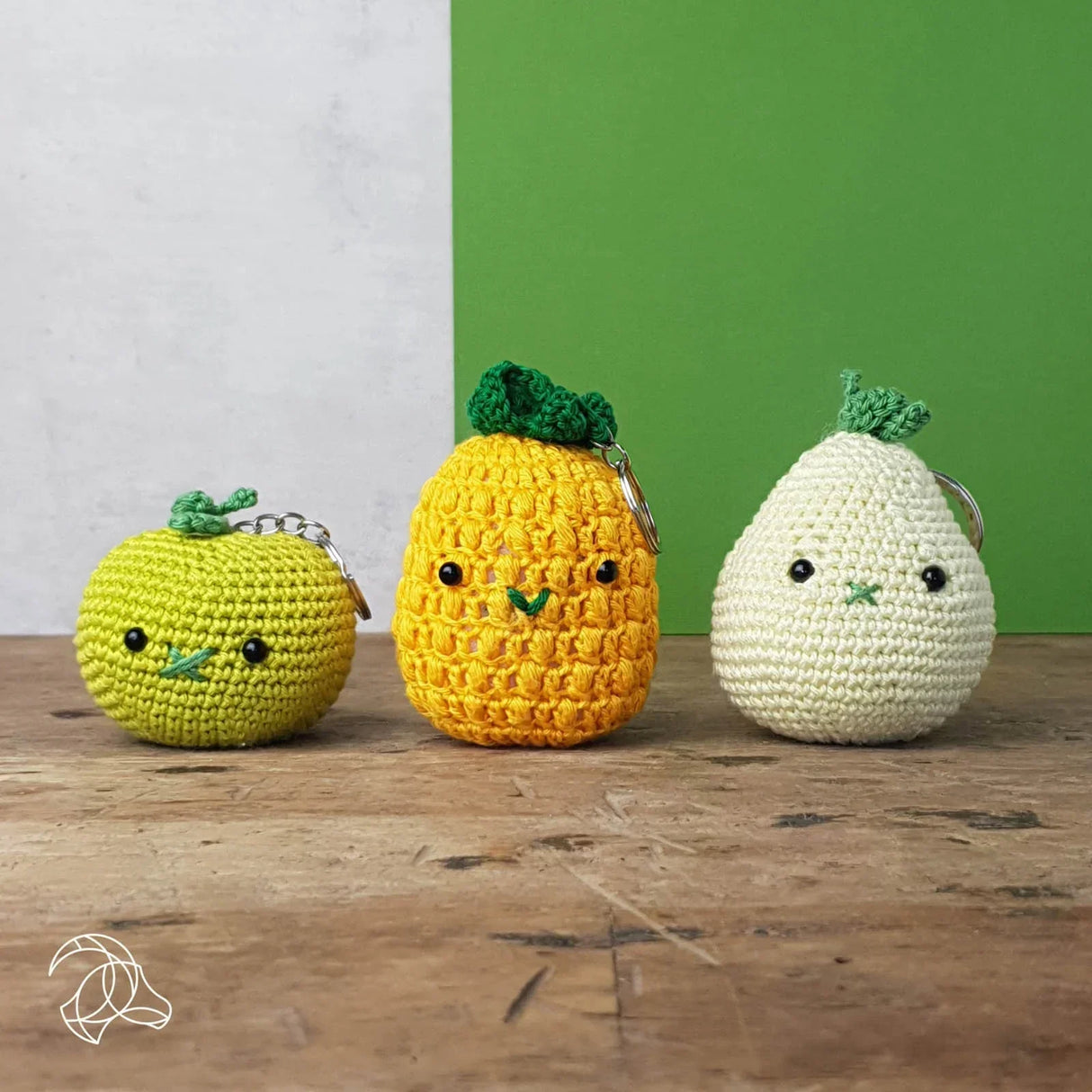Drei gehäkelte Schlüsselanhänger in Form von Apfel Ananas und Birne auf einem Holztisch