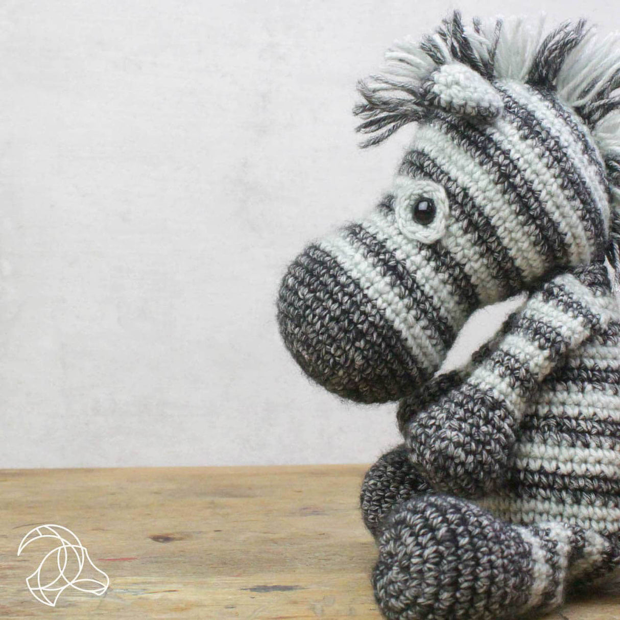 Gehäkeltes Zebra Kuscheltier in grau und weiß auf einem Holztisch