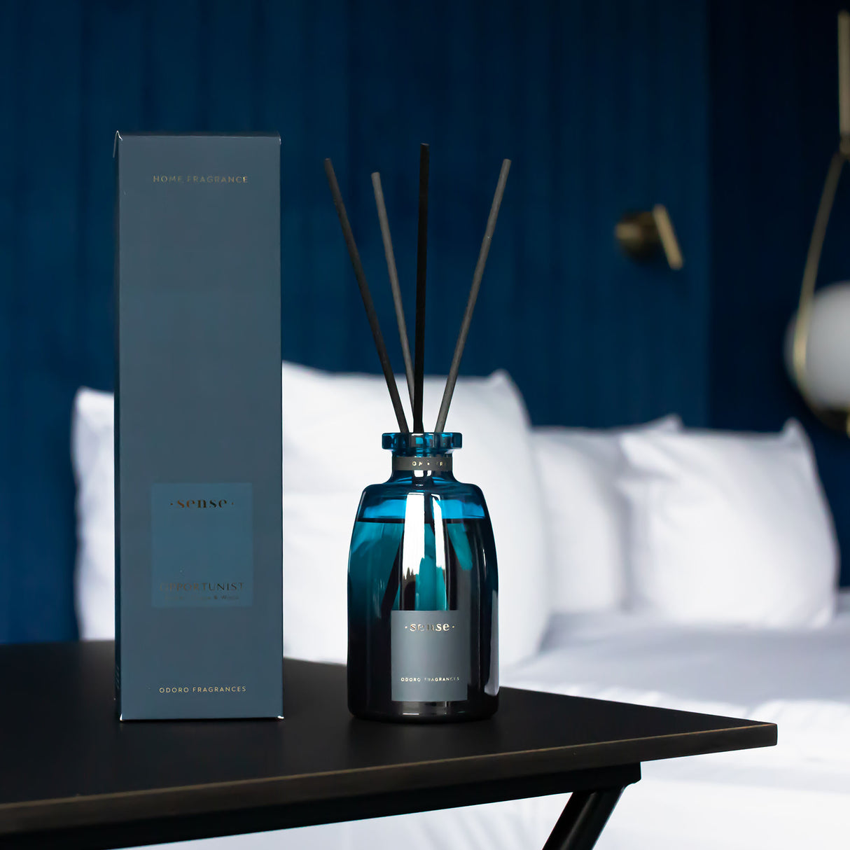Blauer Raumduft Diffuser mit Stäbchen und Verpackung auf einem Tisch vor einem Bett
