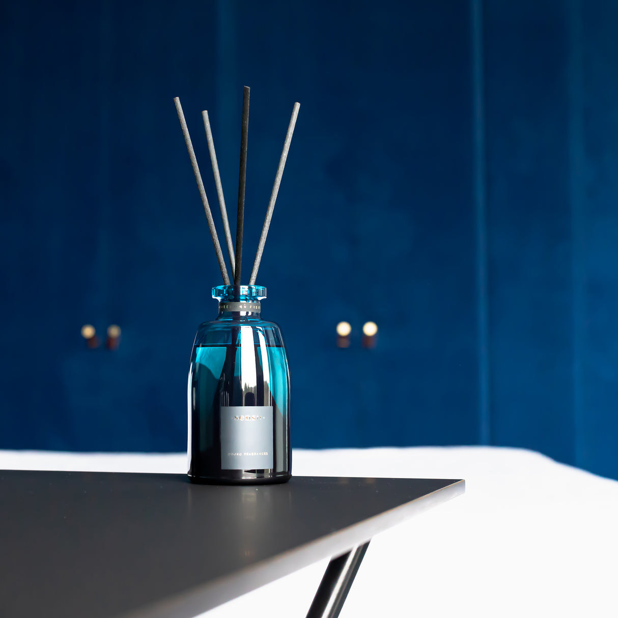 Blauer Duftdiffusor mit Duftstäbchen auf einem Tisch vor blauem Hintergrund