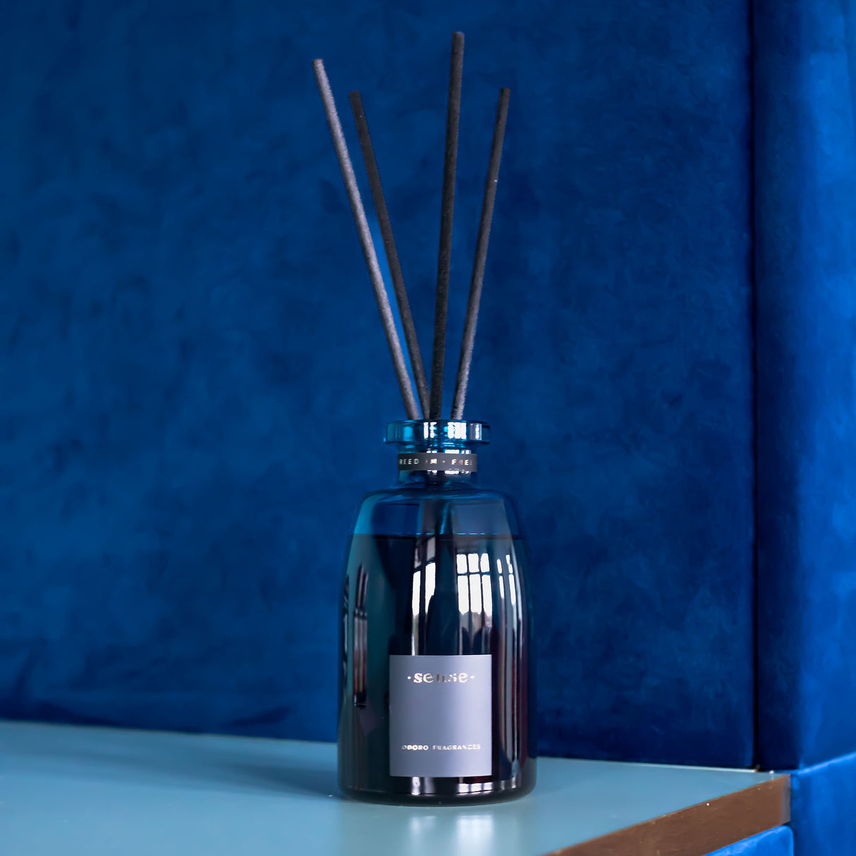 Blauer Duftdiffusor mit schwarzen Stäbchen vor blauem Hintergrund