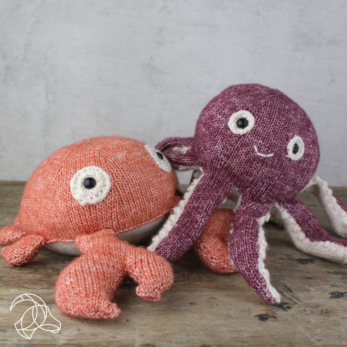 Gestrickte Stofftiere in Form einer Krabbe und eines Oktopus auf einem Holztisch