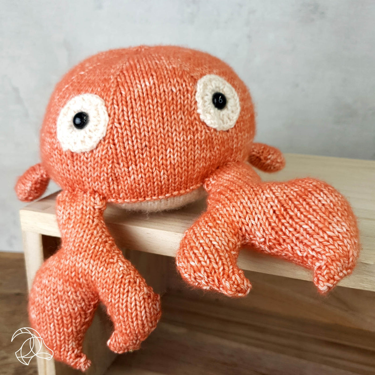 Gestrickte orangefarbene Krabbe als Stofftier mit grossen Augen auf einem Holzregal