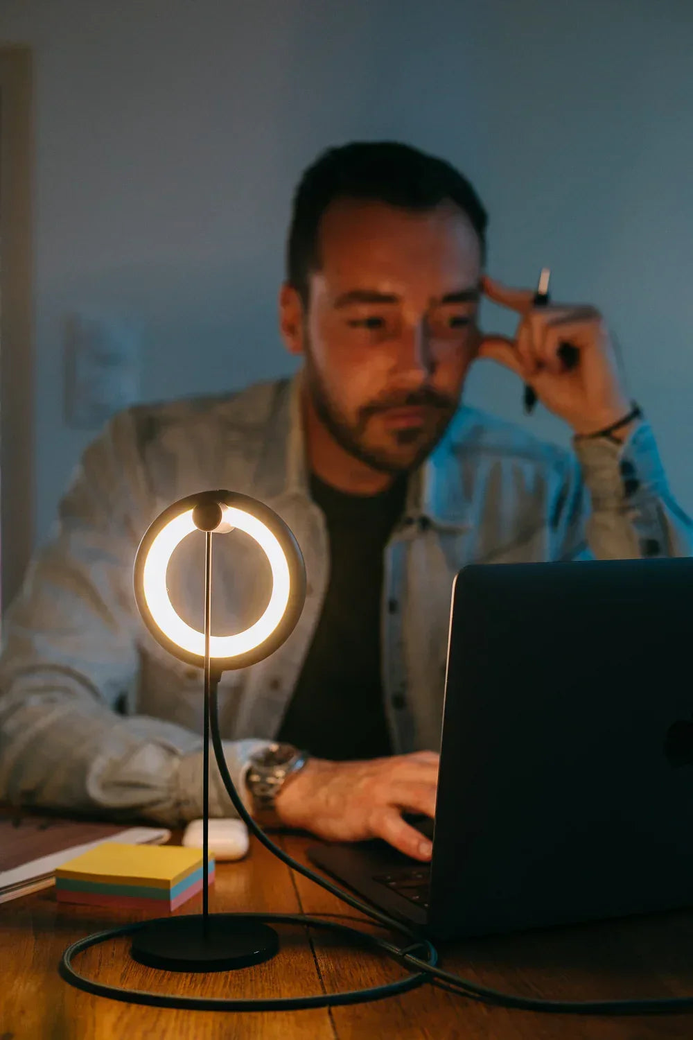 Mann arbeitet an einem Laptop bei Beleuchtung durch eine kleine kreisförmige Schreibtischlampe