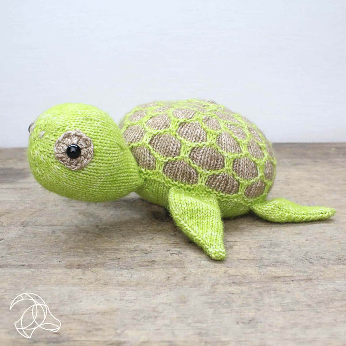 Gestrickte Schildkröte in Hellgrün und Beige auf einem Holztisch