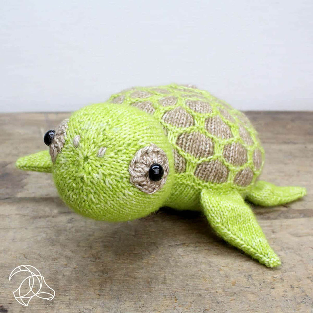 Gestrickte Schildkröte in Hellgrün und Beige auf einem Holztisch