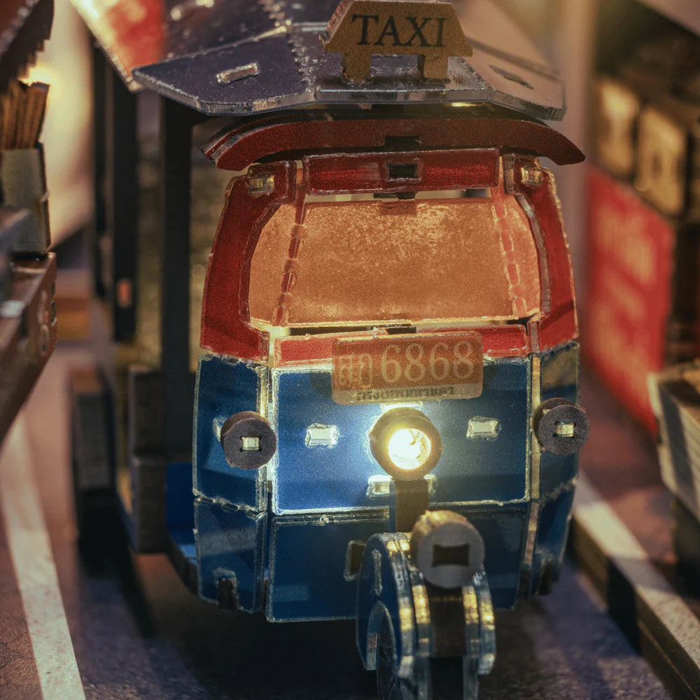Nahaufnahme eines Miniatur-Tuk-Tuks mit leuchtendem Scheinwerfer und Taxischild