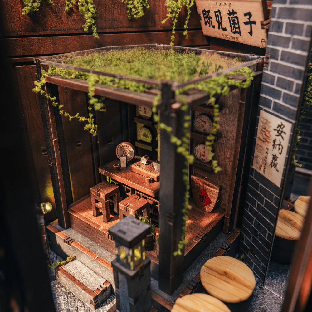 Miniatur-Teehaus mit Holztisch, Hockern und Regalen mit Teedosen, umgeben von grünen Ranken