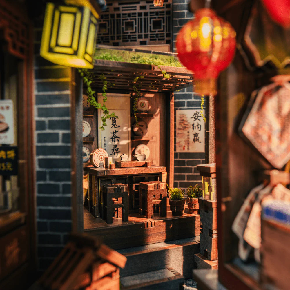 Miniatur-Teehaus mit Holztisch, Hockern und Geschirr, umgeben von Ziegelwänden und Laternen