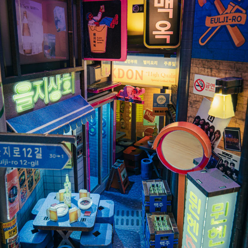 Miniatur-Straßenszene mit beleuchteten Schildern, Tischen und Stühlen, Bierflaschen und Kisten