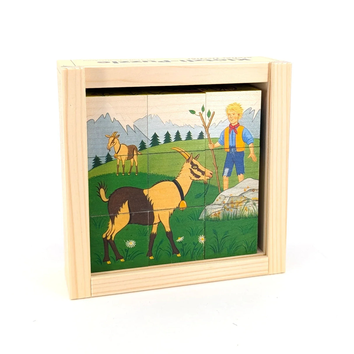 Holzpuzzle mit Ziegen und einem Jungen auf einer Wiese vor Bergen