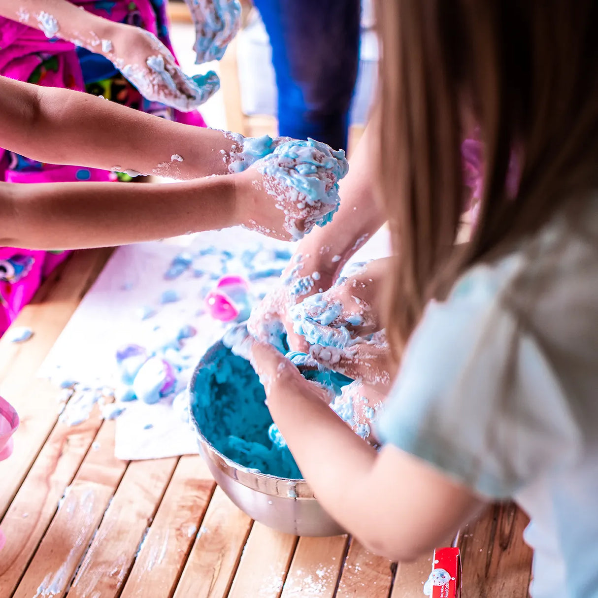 Kinderhände spielen mit blauem Schleim in einer Schüssel auf einem Holzboden