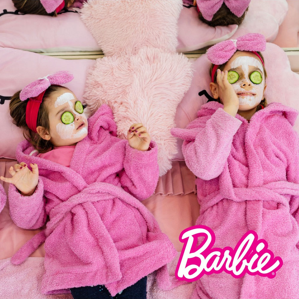 Zwei Mädchen in rosa Bademänteln mit Gesichtsmasken und Gurkenscheiben auf den Augen