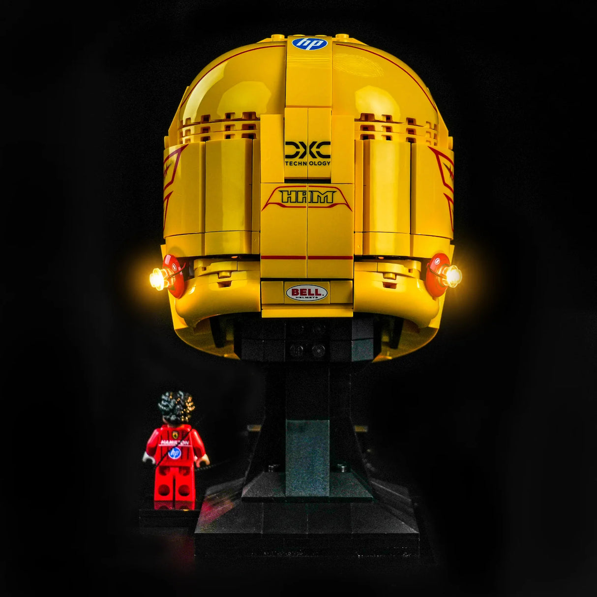 Rückansicht des gelben LEGO Scuderia Ferrari HP Helms mit zwei leuchtenden BrickBling LEDs an den Seiten und einer Lewis Hamilton Minifigur im roten Rennanzug.