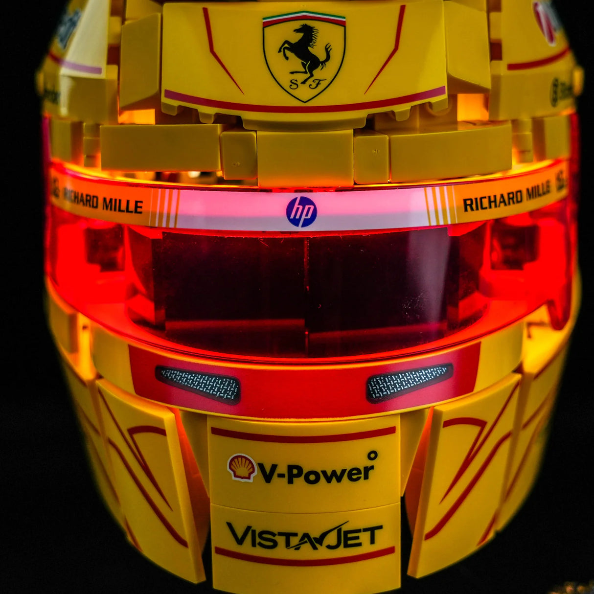 Frontansicht des beleuchteten LEGO Lewis Hamilton Ferrari Helms mit rot leuchtendem Visier, Ferrari-Logo, HP-Branding und V-Power Aufkleber durch BrickBling LED-Kit.