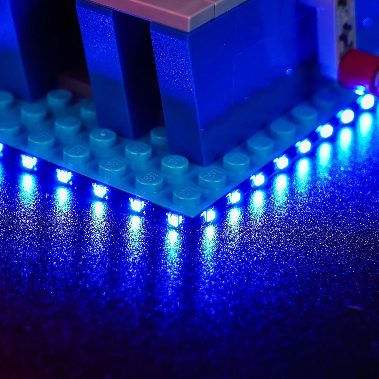 BrickBling LED-Lichtset für LEGO 43307 – Nahaufnahme einer flexiblen, blau leuchtenden LED-Streifen-Beleuchtung an der Unterseite der Pizza Planet LEGO-Bodenplatte.