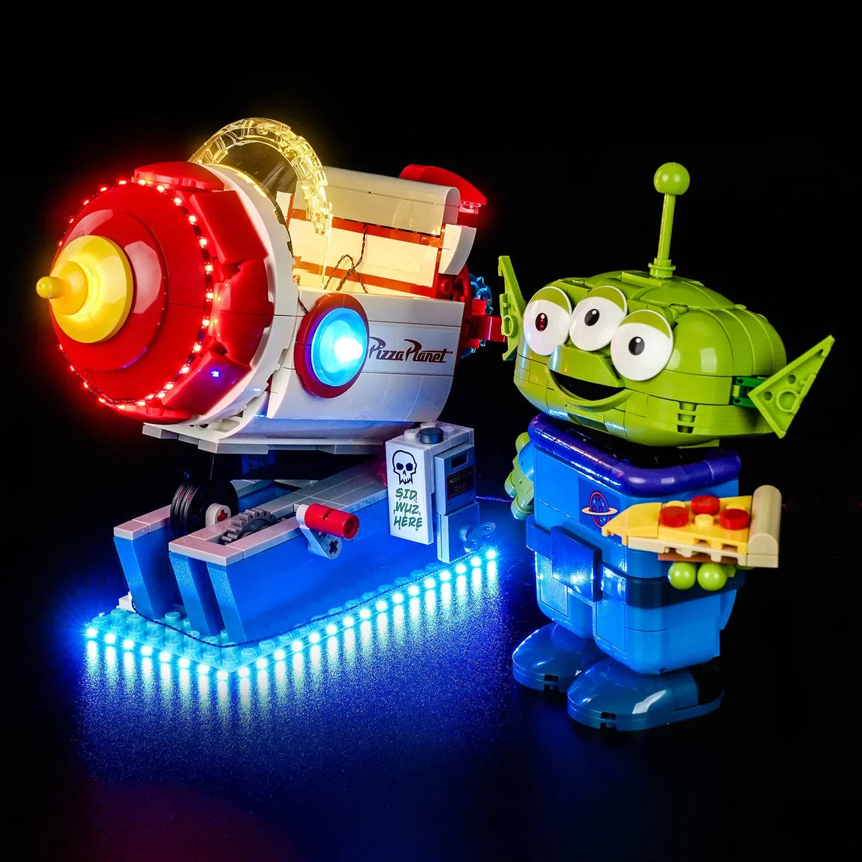 Beleuchtete LEGO Pizza Planet Raketenfahrt von BrickBling mit danebenstehender Toy Story Alien LEGO-Figur auf schwarzem Hintergrund.