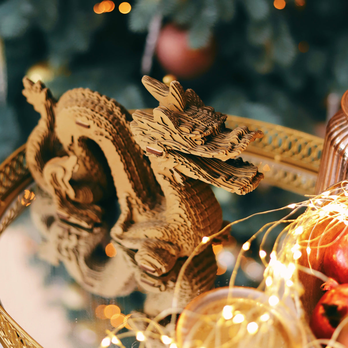 Drachenfigur aus Wellpappe auf einem goldenen Tablett vor einem Weihnachtsbaum
