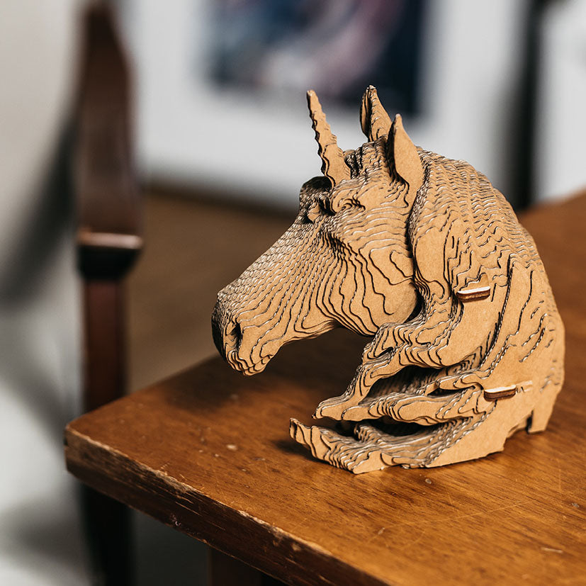 Skulptur eines Einhornkopfes aus geschichtetem braunem Karton auf einem Holztisch