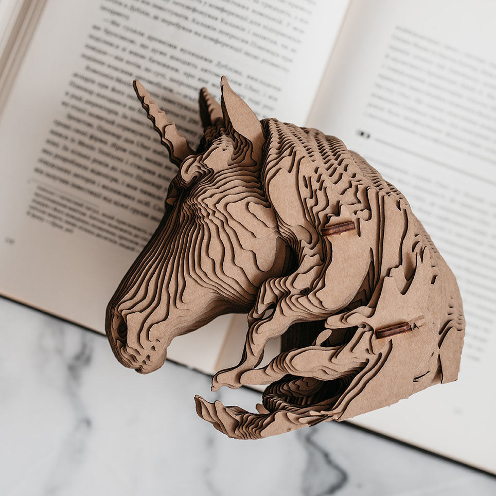 Einhorn Skulptur aus geschichtetem Karton vor einem aufgeschlagenen Buch