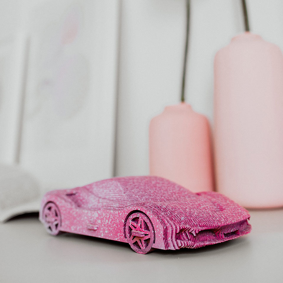 Rosa 3D gedrucktes Modellauto auf einem Tisch vor zwei rosa Vasen