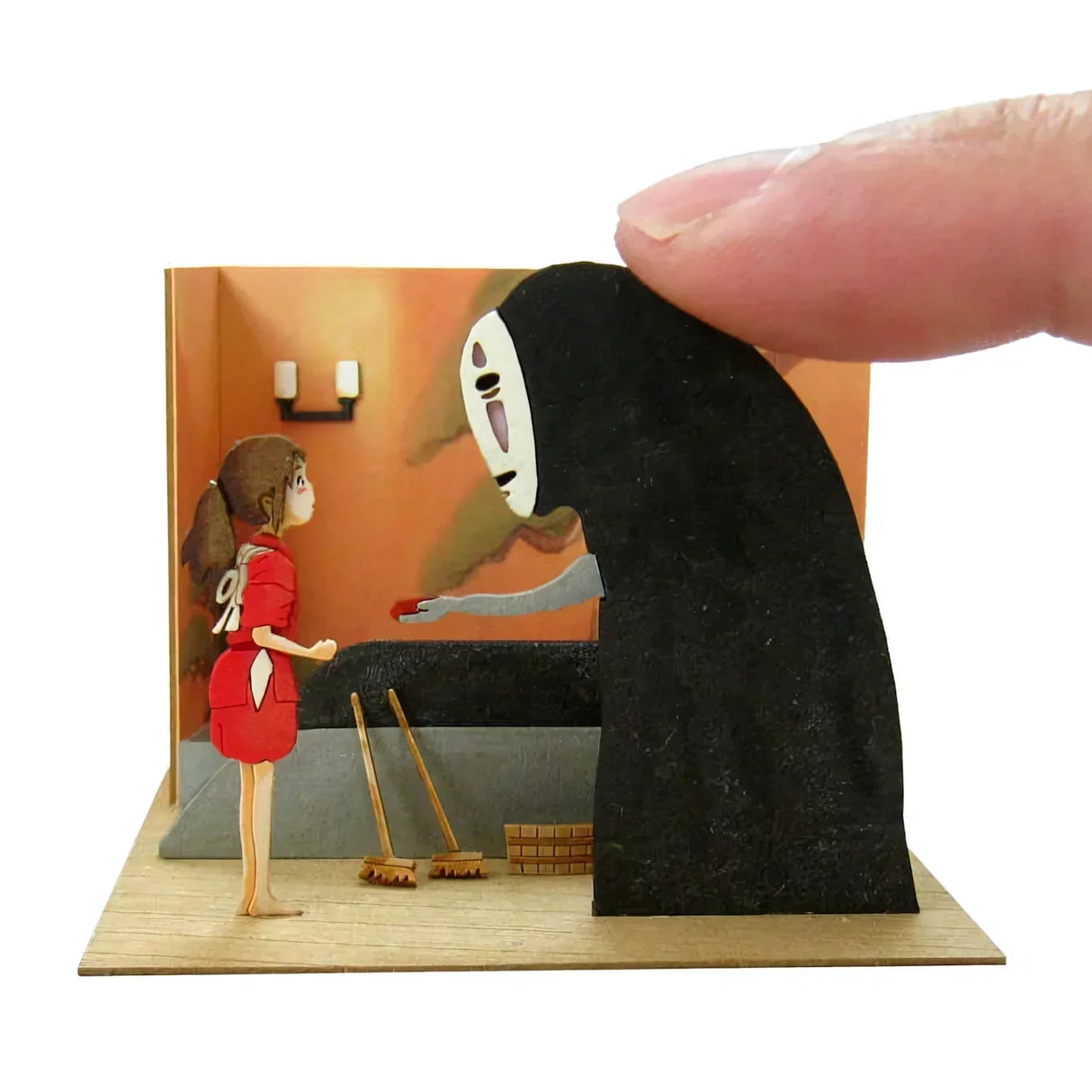 Ein Finger hält eine Figur von Ohngesicht, die Chihiro einen roten Gegenstand anbietet