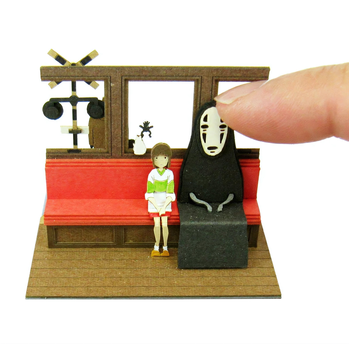 Finger berührt No-Face Figur neben Chihiro auf roter Bank
