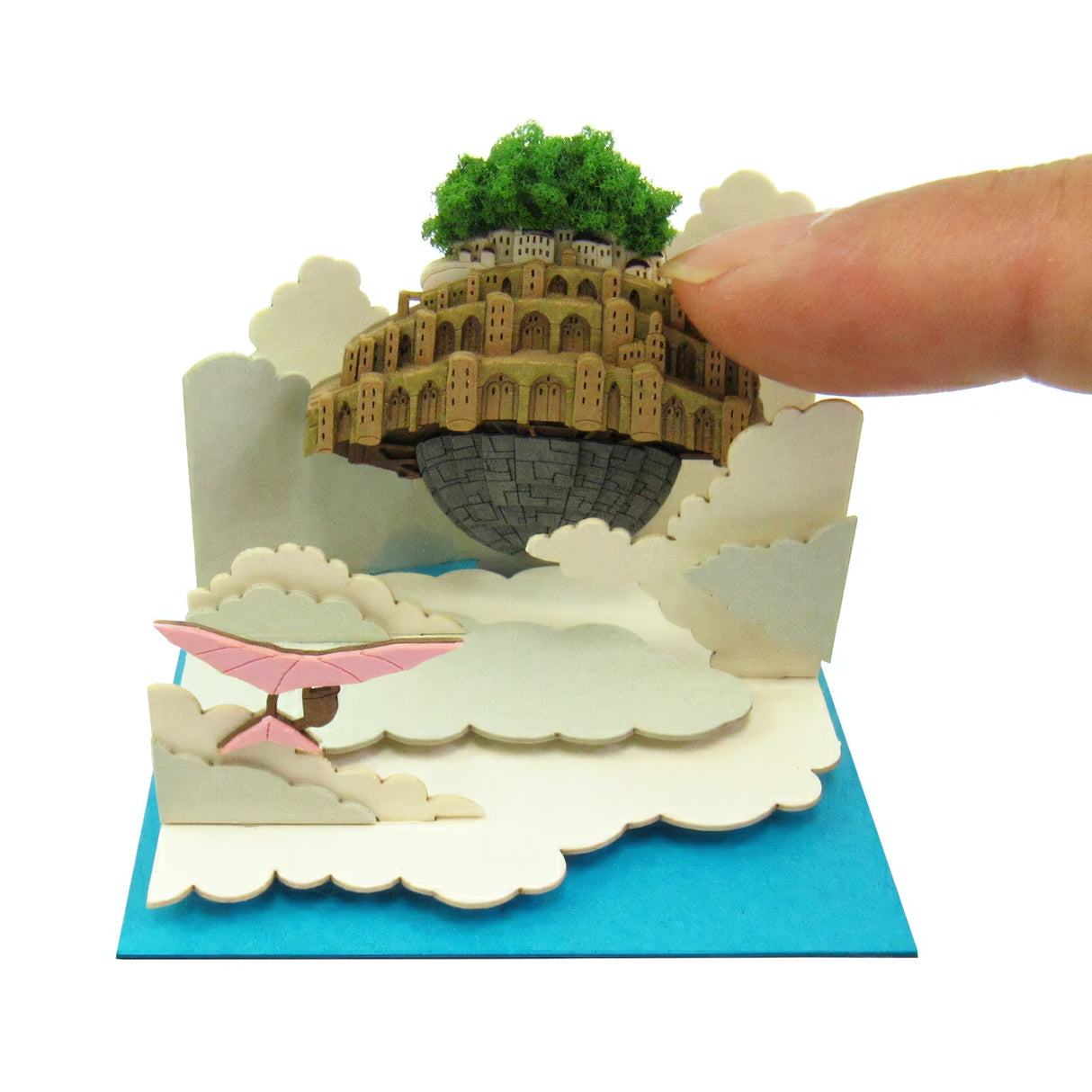 Miniaturmodell einer schwebenden Stadt mit Bäumen und Gebäuden, umgeben von Wolken, ein Finger berührt die Stadt