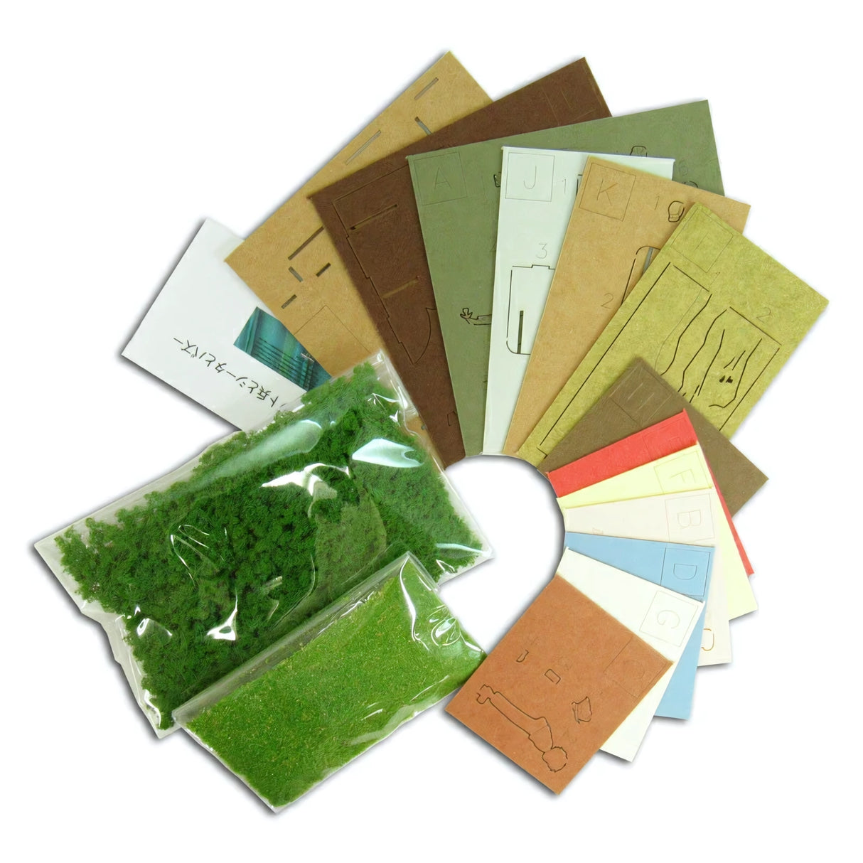 Modellbausatz mit grünen Streumaterialien und farbigen Kartonbögen