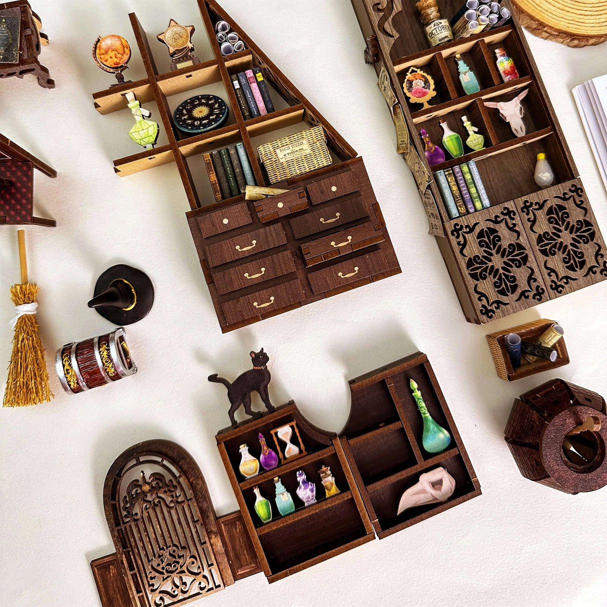 Drei Miniatur-Regale mit Tränken, Büchern und magischen Gegenständen, daneben ein Besen und ein Hexenhut