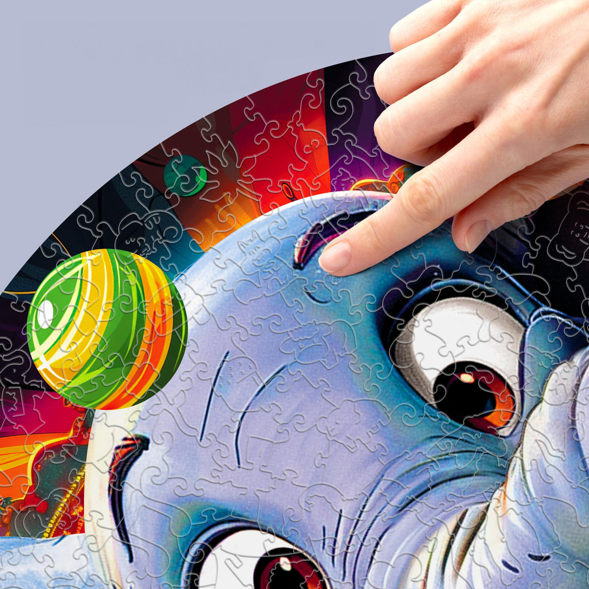 Hand legt ein Puzzleteil auf ein blaues Monster mit großen Augen und einem gestreiften Ball