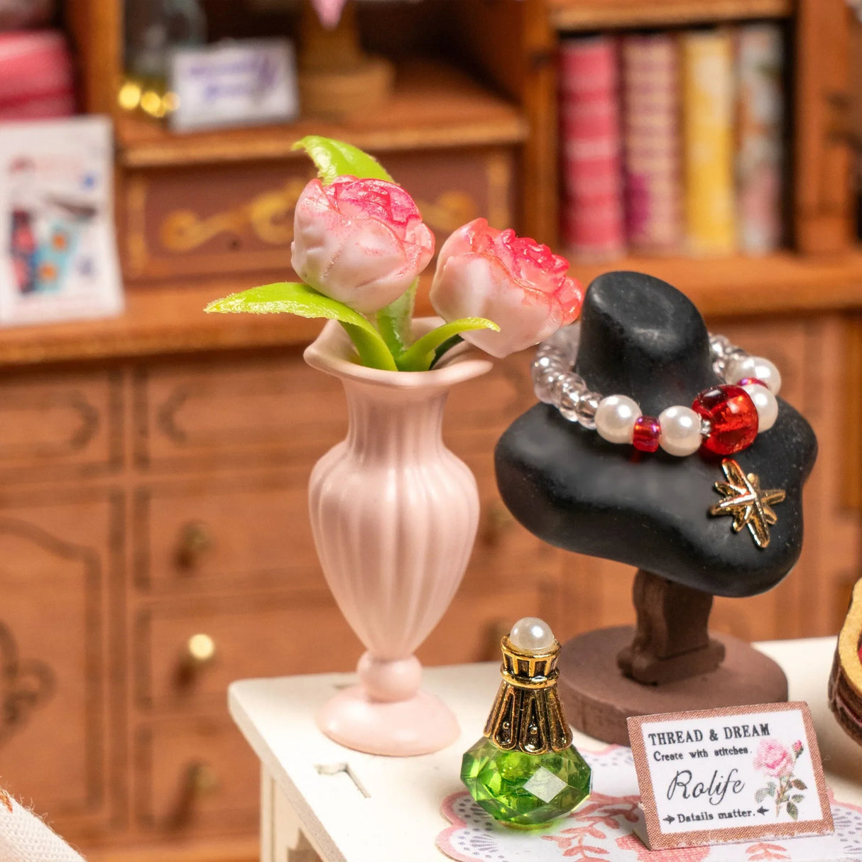 Miniatur-Vase mit rosa Blumen, Schmuckständer mit Perlenarmband und Parfümflasche