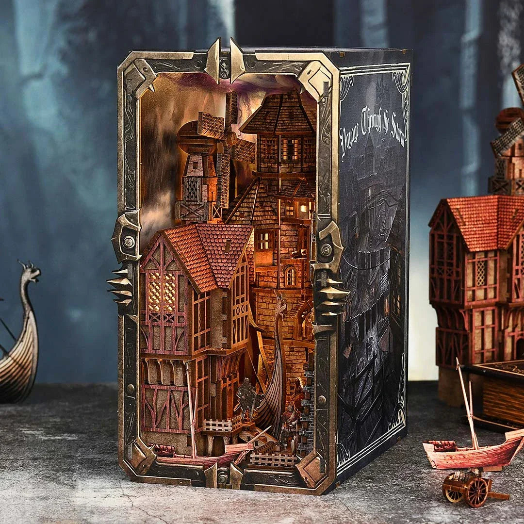 Diorama eines mittelalterlichen Dorfes mit beleuchteten Häusern und Booten in einem Buchrahmen