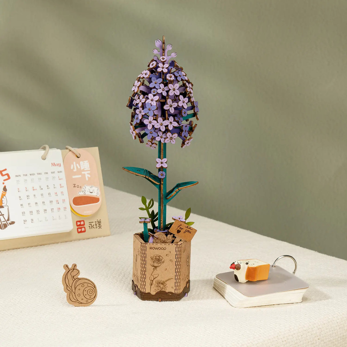 Holzsteckbausatz einer lila Blume im Topf mit Kalender und Schneckenfigur auf einem Tisch