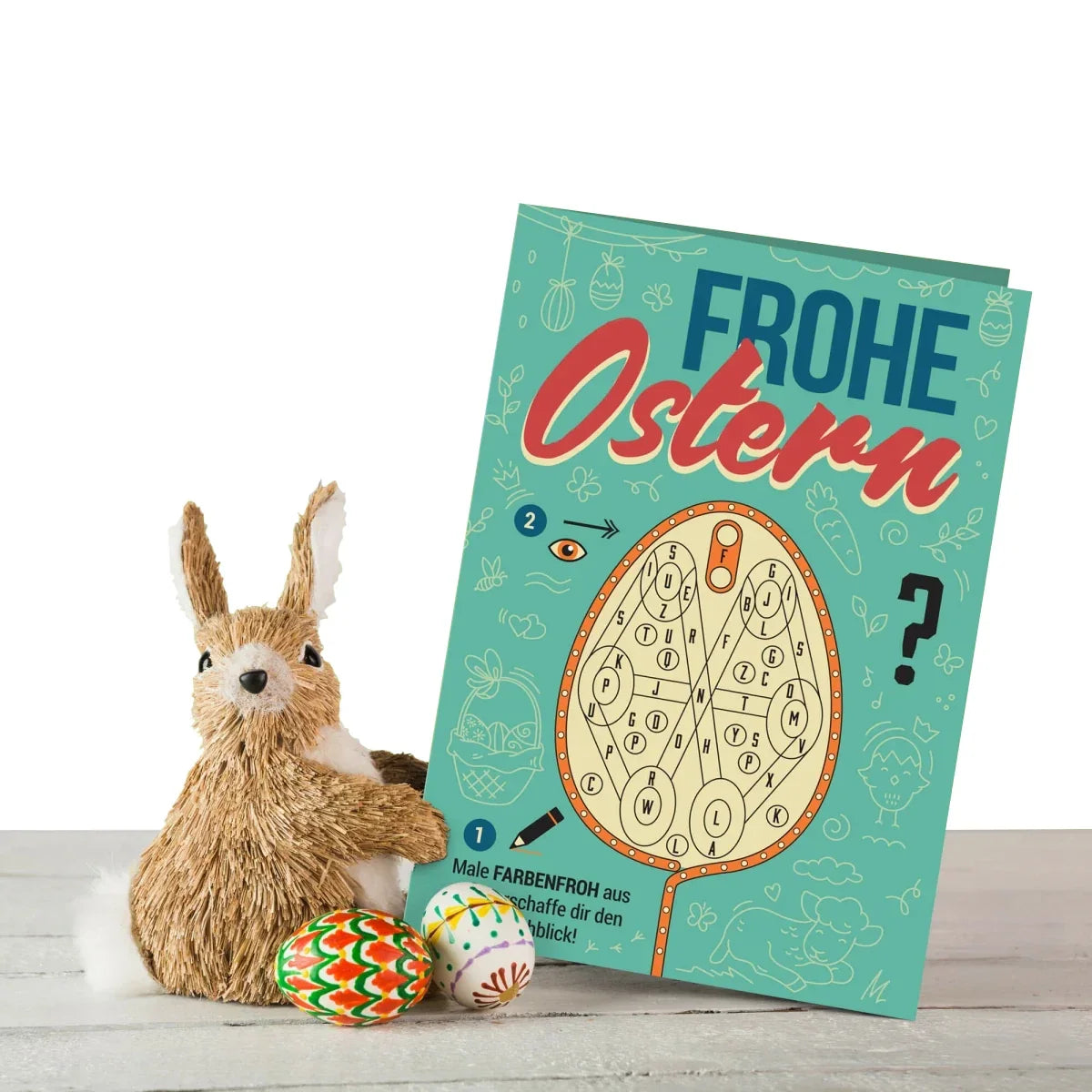 Osterhase aus Bast mit zwei bemalten Eiern und einem Oster-Malbuch