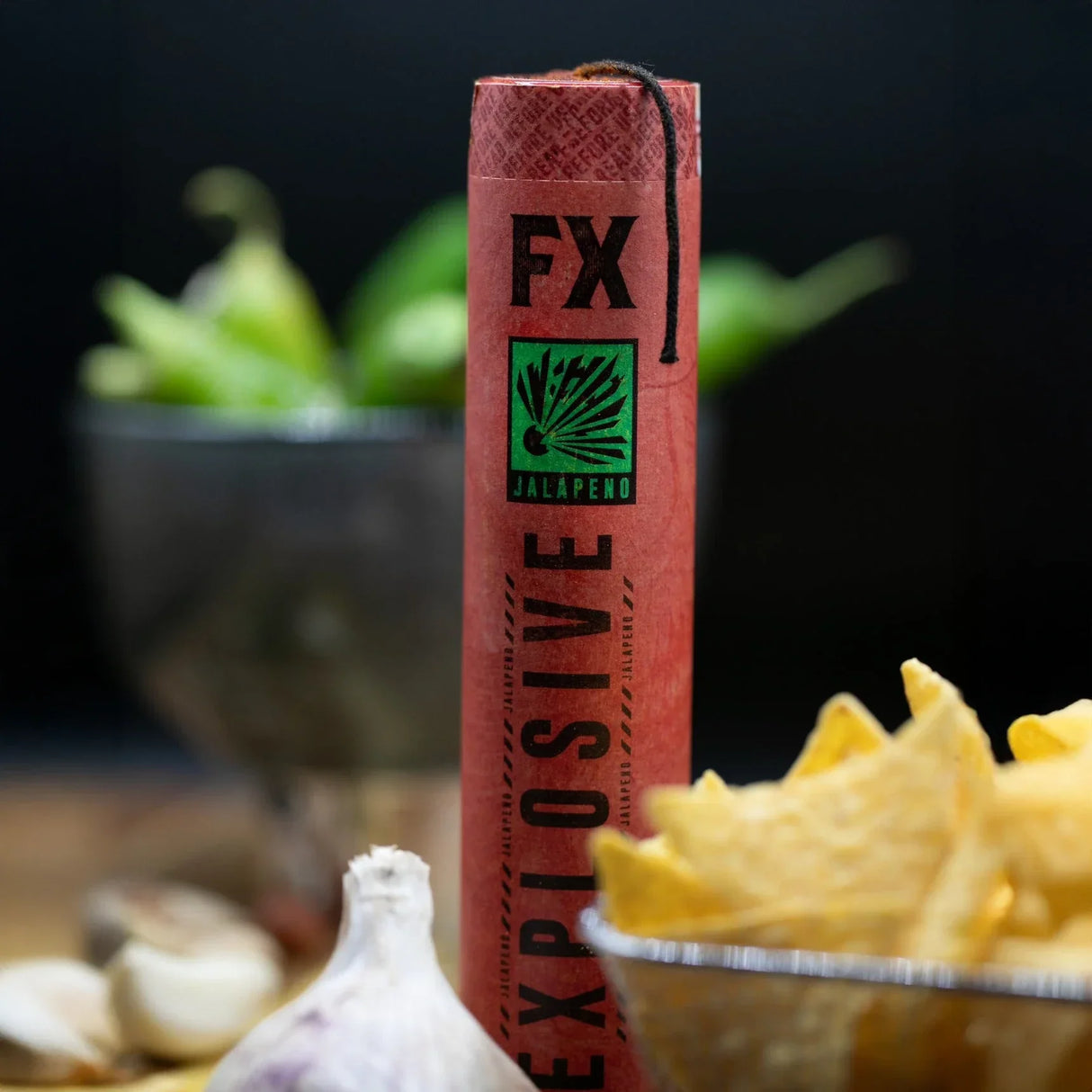 Rote FX Explosive Jalapeno-Verpackung mit schwarzem Docht, umgeben von Knoblauch, Nachos und Jalapenos