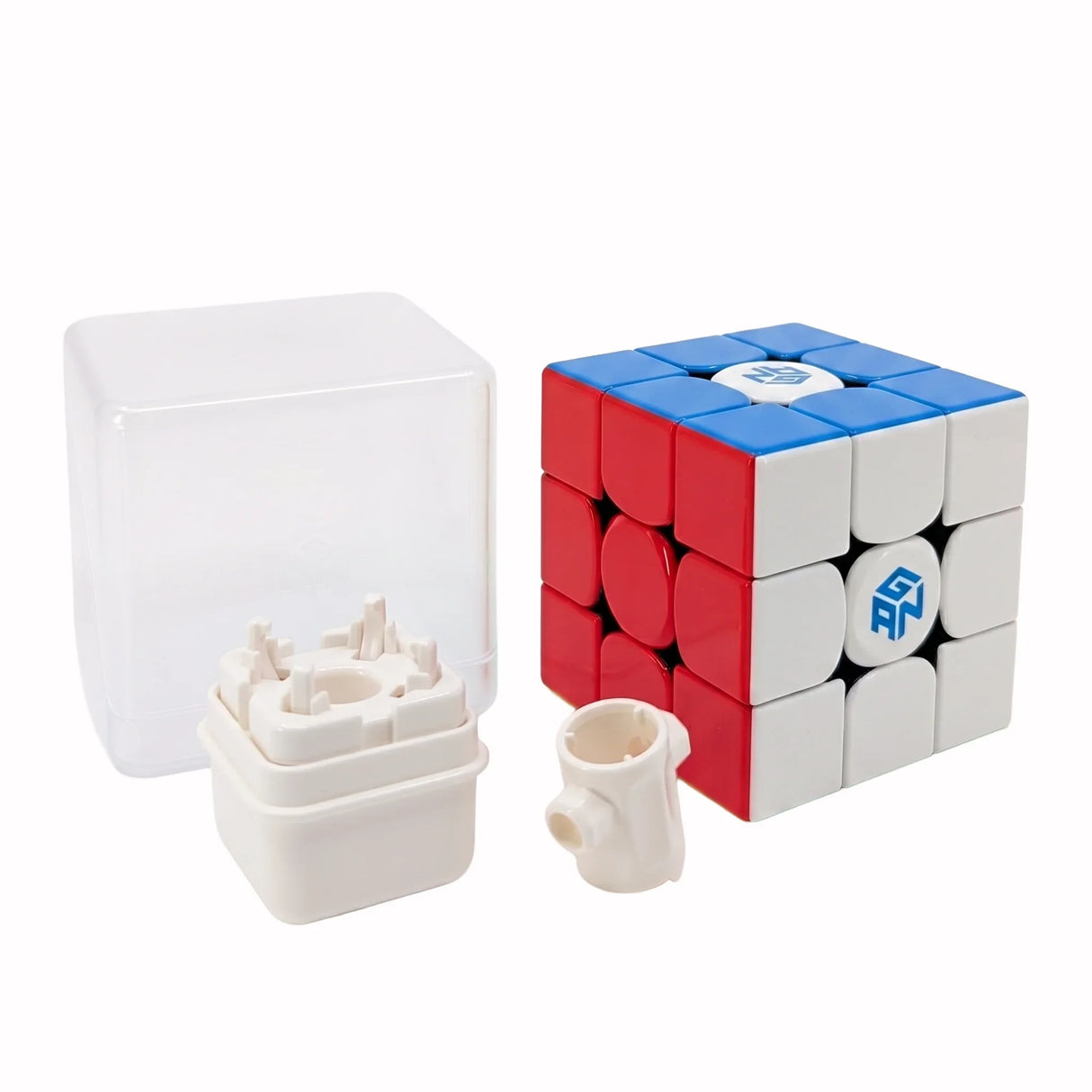 Rubikswürfel mit roter, blauer und weißer Seite, daneben eine transparente Box und zwei weiße Kunststoffteile