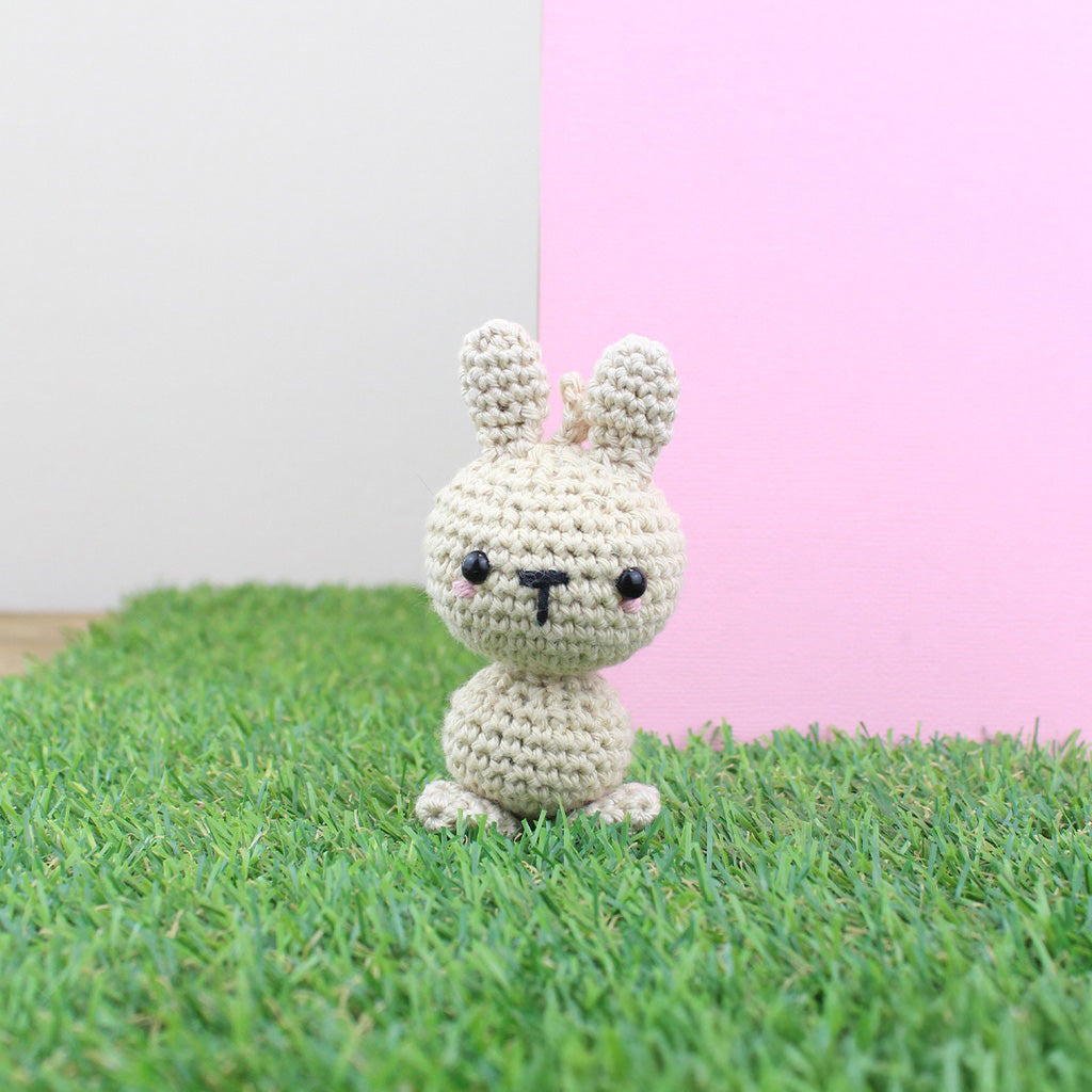 Gehäkelter Hase auf grünem Gras vor rosa und weißem Hintergrund