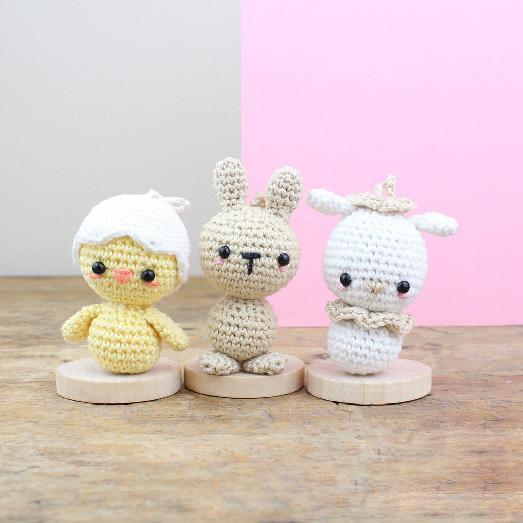 Drei gehäkelte Figuren: ein gelbes Küken, ein beiger Hase und ein weißes Lamm auf Holzsockeln