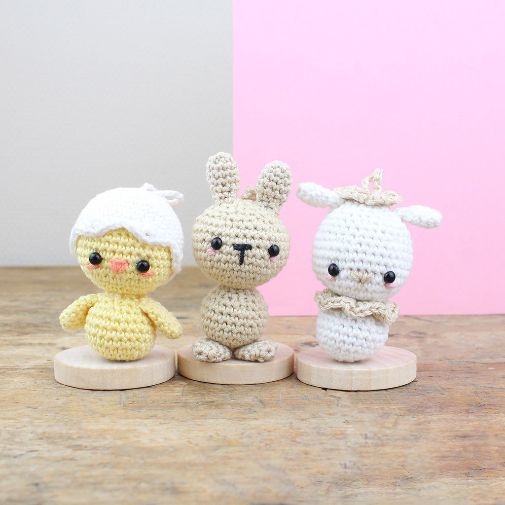 Drei gehäkelte Figuren: ein Küken, ein Hase und ein Lamm auf Holzsockeln
