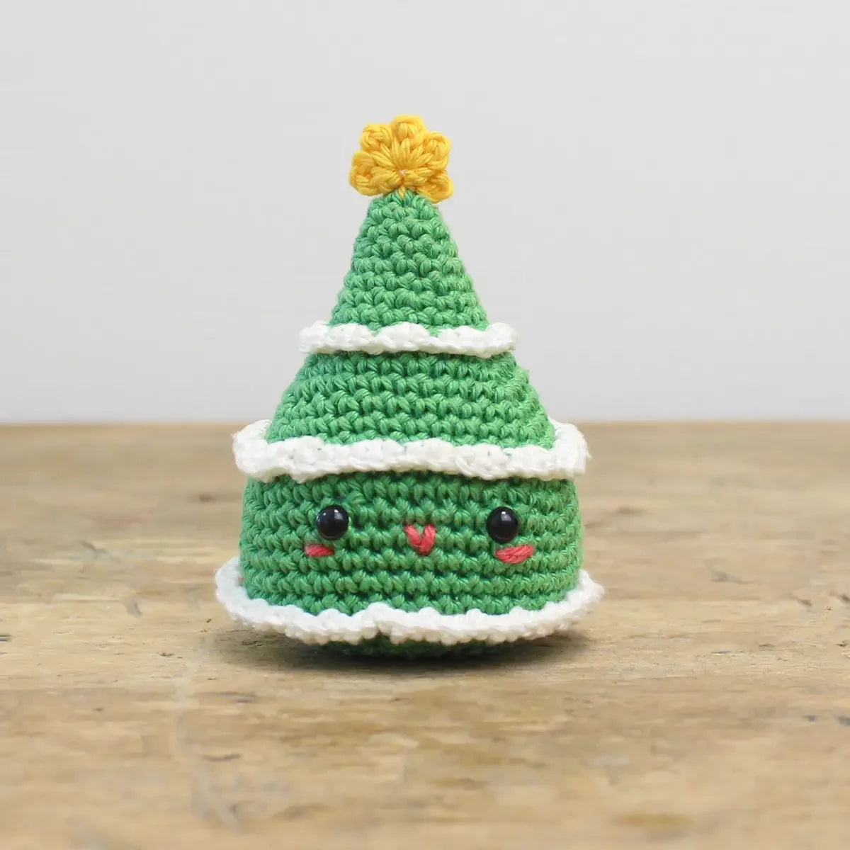 Gehäkelter Weihnachtsbaum mit Gesicht und gelbem Stern auf einem Holztisch
