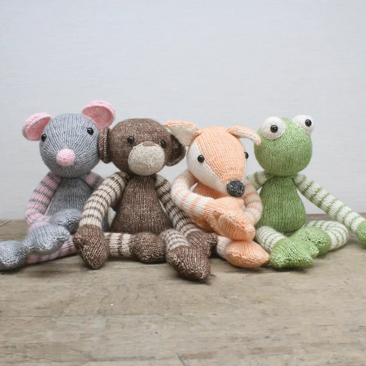 Vier handgestrickte Stofftiere in Form einer Maus, eines Affen, eines Fuchses und eines Frosches nebeneinander