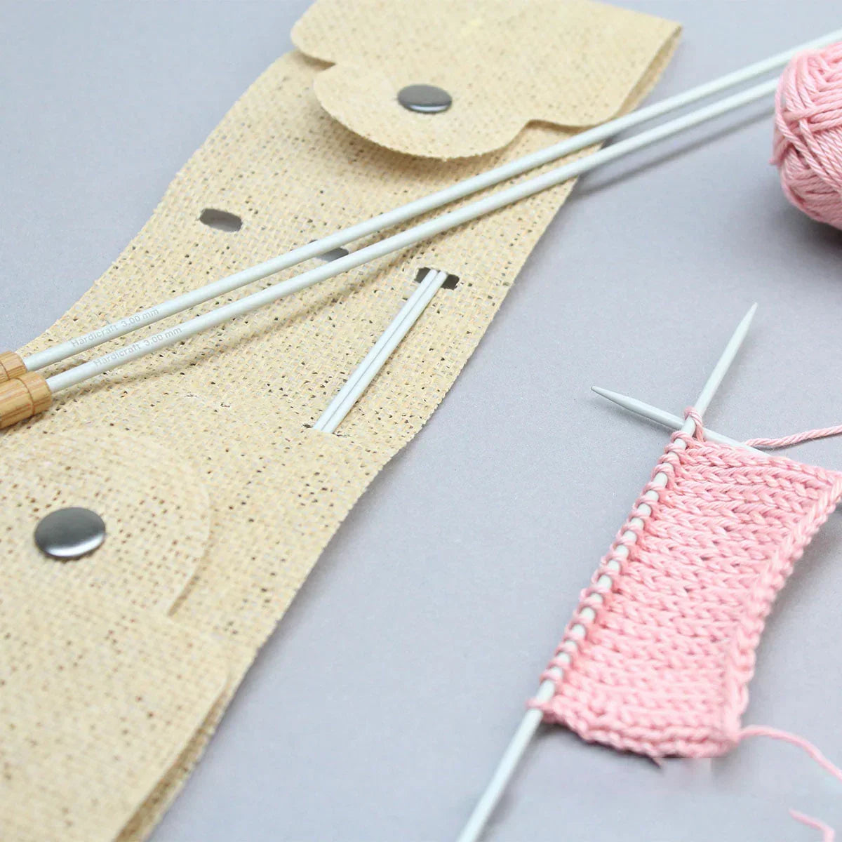 Stricknadelset mit beigem Etui und rosa Garn auf grauem Untergrund