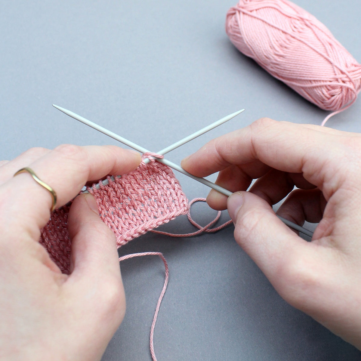 Hände beim Stricken mit rosa Garn und Stricknadeln