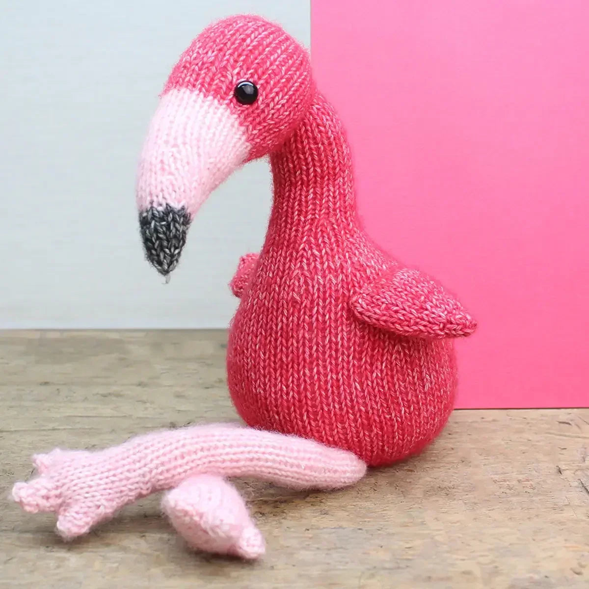 Gestrickter Flamingo aus rosa Wolle mit hellem Schnabel auf einem Holztisch