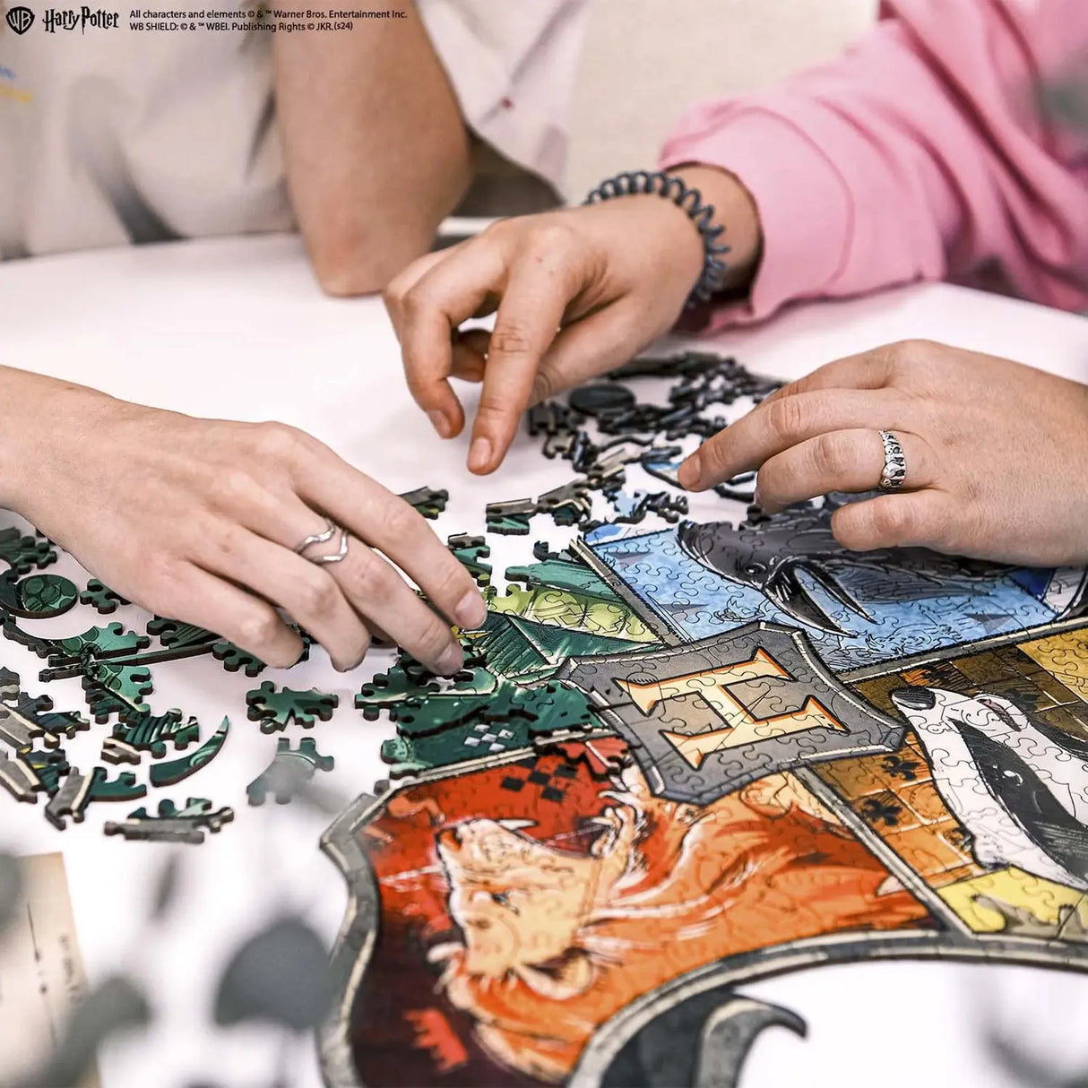 Zwei Personen legen ein Harry Potter Wappen-Puzzle mit den Häusern Gryffindor, Hufflepuff, Ravenclaw und Slytherin